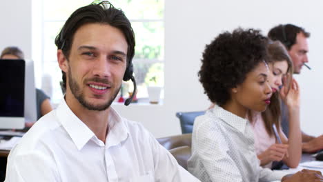 hombre con auriculares en una oficina de plan abierto sonríe a la cámara