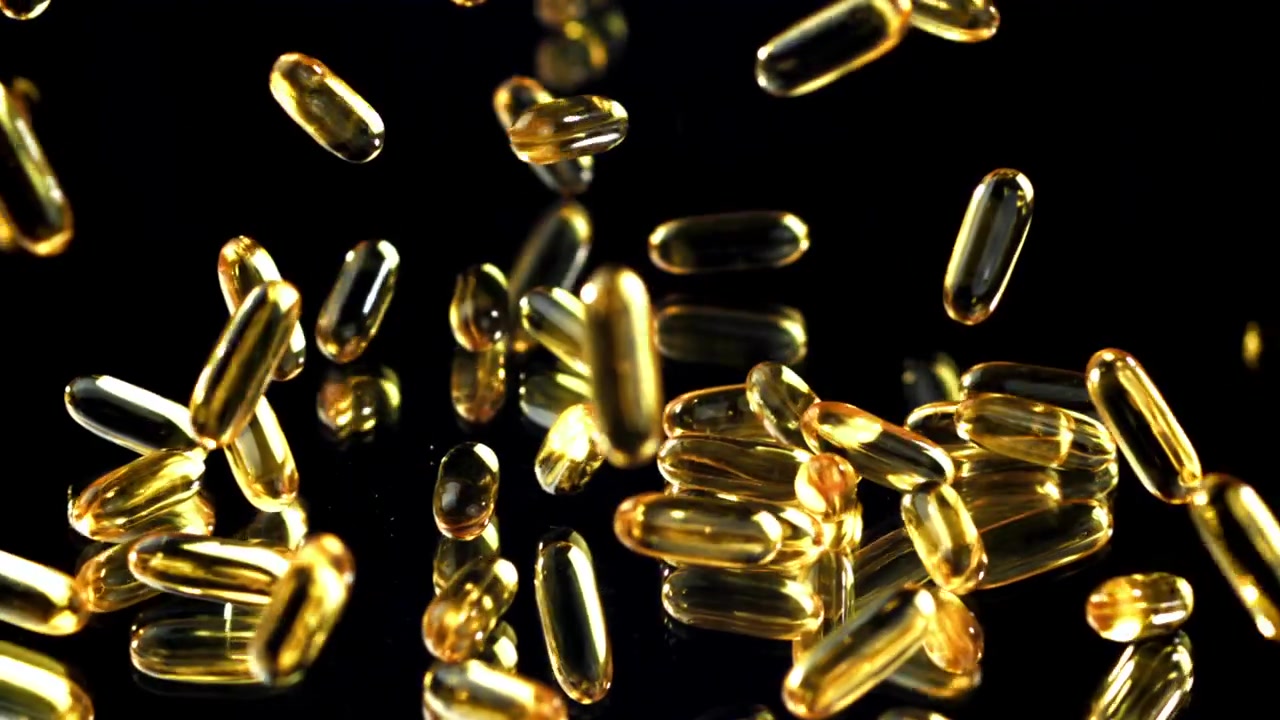 Capsule dorate di Omega 3 che cadono al rallentatore su una superficie nera riflettente
