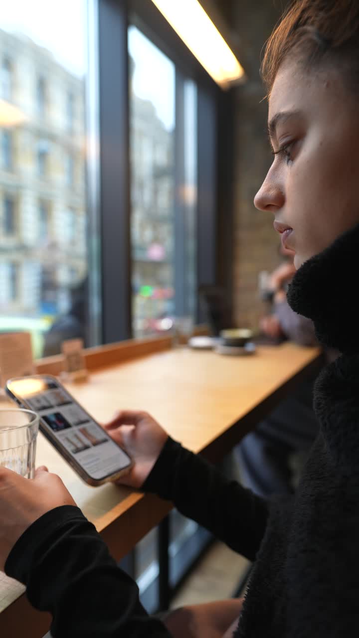 Young Woman in a Cafe Using Smartphone and Drinking Water