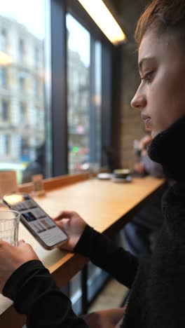 mujer joven en un café usando un teléfono inteligente y agua potable