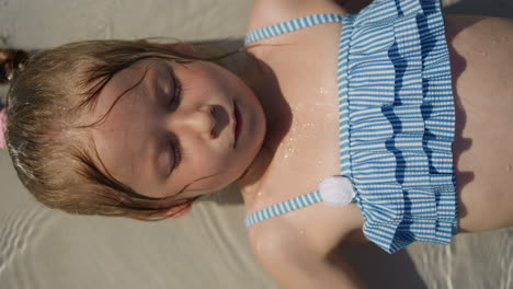 Calm little girl lies in clear shallow pool with closed eyelids
