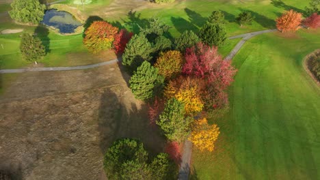 orbiting overhead view of a golf course with numerous trees changing color with the seasons