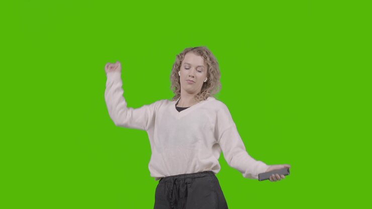 Scatto in studio di una giovane donna che ascolta musica sul cellulare e balla su sfondo verde 5