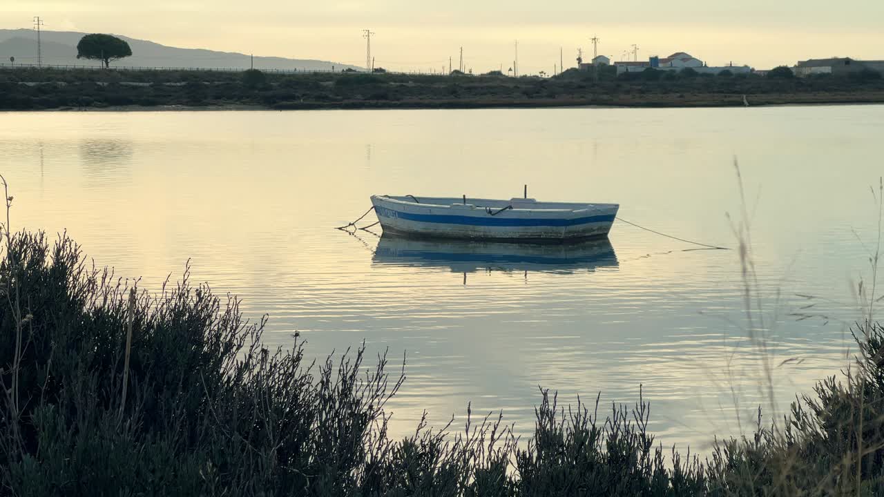 Безмятежный снимок лодки, стоящей на якоре в водном канале, ведущем к морю, в теплых лучах заката