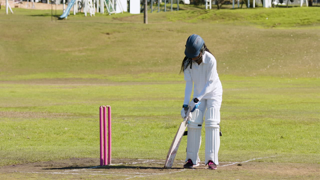 Playing cricket, female batter in protective gear preparing to hit ball