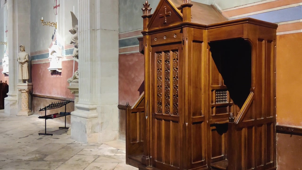 Traditional wooden confessional booth inside historic church interior in France next to holy statues
