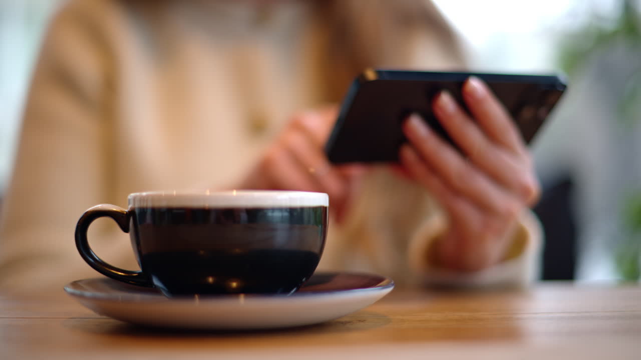 Woman drinking latte coffee while watching content on smartphone