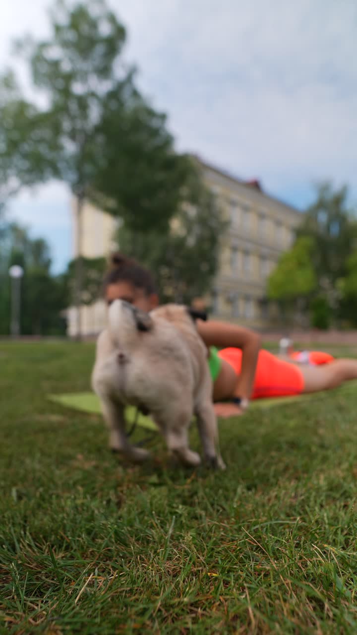 Donna che fa yoga in un parco con il suo carlino