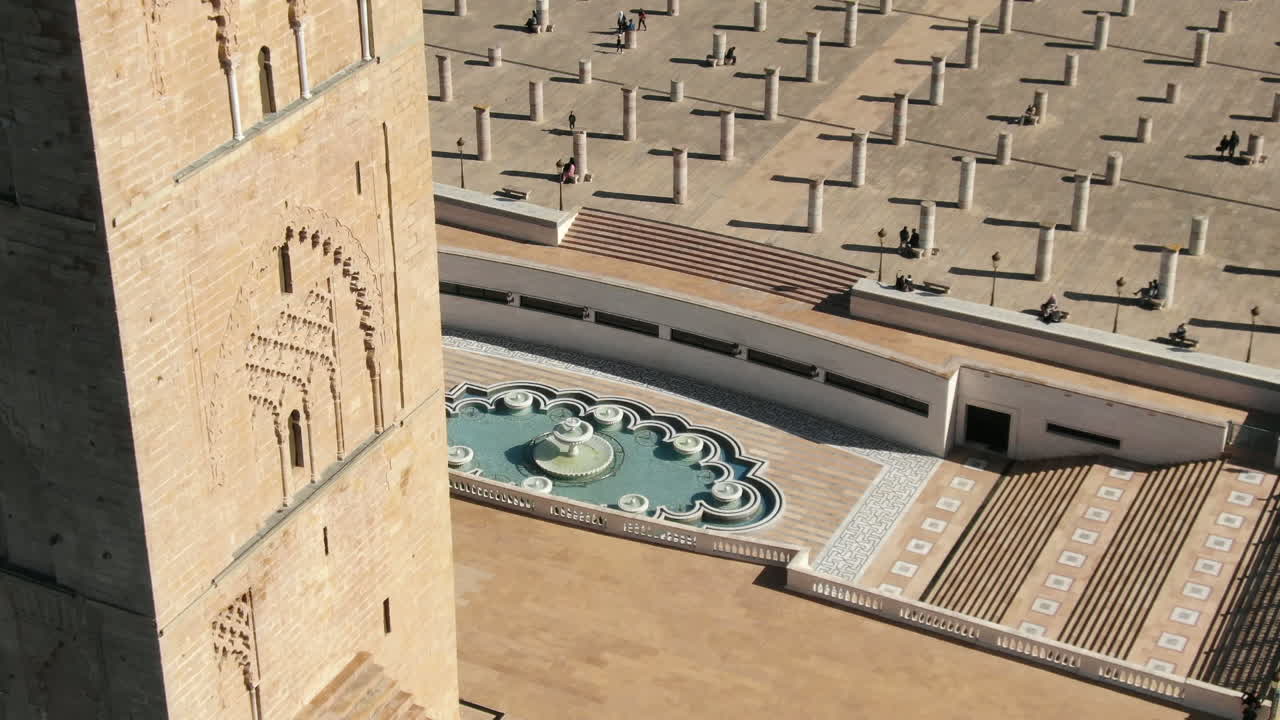 Detaljeret HD-nærbillede af det historiske Hassan Tårn i Rabat, med indviklede Almohad-udskæringer, søjlepladsen og et geometrisk springvand i baggrunden. Fanger essensen af den moriske stil