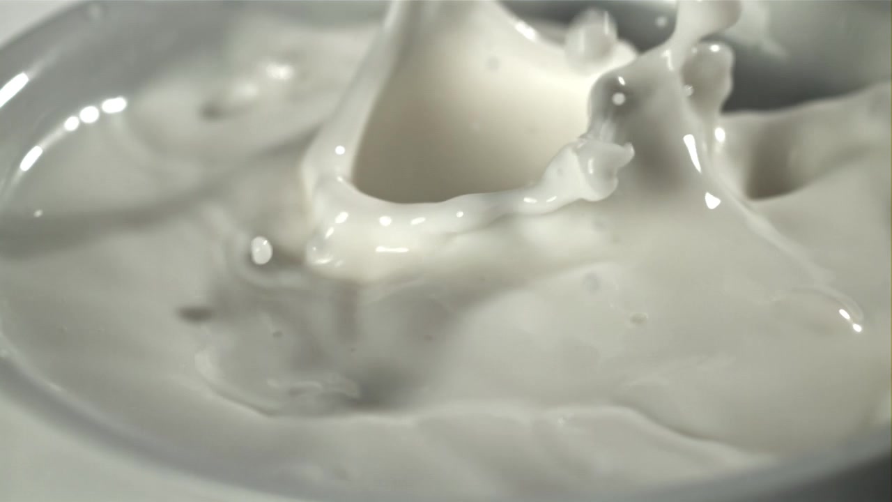 Slowmotion mælkedråber sprøjter ned i hvid væske