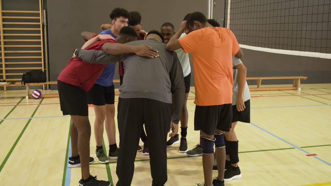 Squadra di pallavolo maschile multietnica che risponde al segnale dell'allenatore, radunandosi per un discorso motivazionale vicino alla rete in palestra.