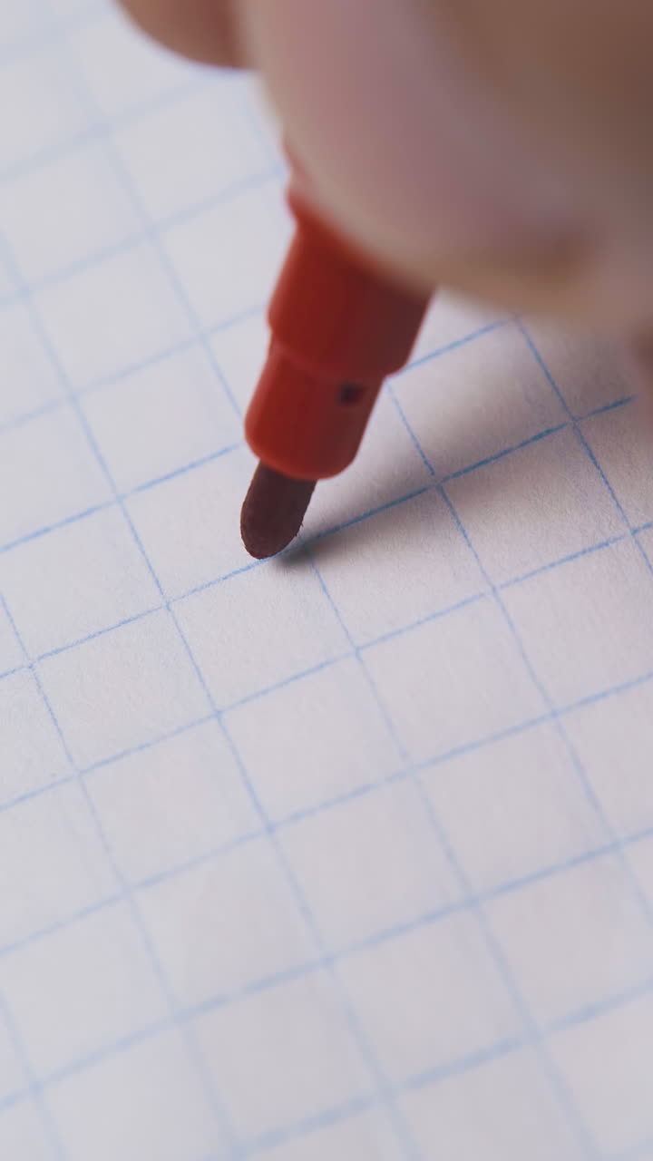 young person draws circle with red marker on blank checkered paper sheet extreme close view
