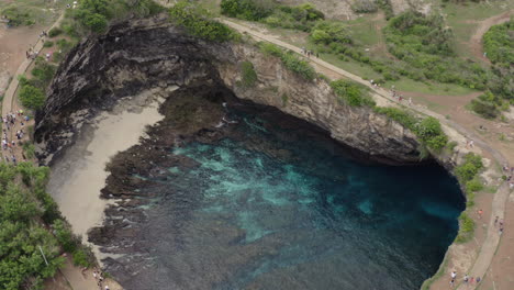 tourists walking along the walkway around a cove in the coast of broken beach, nusa penida, bali, indonesia. aerial shot.