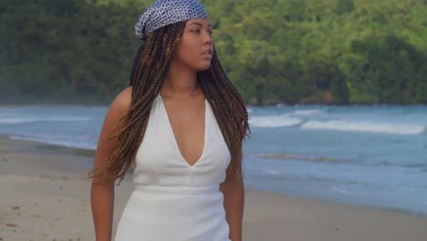 a young woman walking on the beach in a beach dress with ocean waves crashing in the background on a sunny day