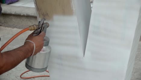 close-up of a hand painting in white color a wooden surface with a spray gun