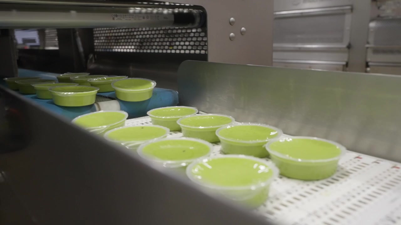 Guacamole containers moving through automated sealing machine in industrial processing plant