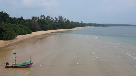 Vista-Aérea-Volando-A-Lo-Largo-De-La-Playa-Vacía-De-Ao-Kao-En-Koh-Mak-Pasando-Por-Un-Solitario-Barco-Pesquero-Amarrado-En-La-Arena