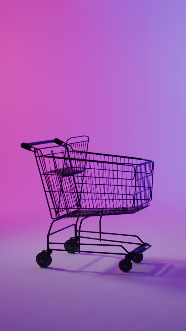 Vertical video of shopping trolley with copy space over pink neon background