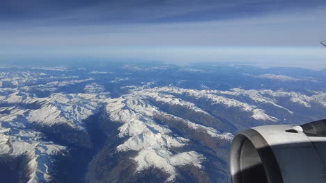 looking through the window aircraft during flight and seeing a snow covered european alps mountain range with blue sky without clouds