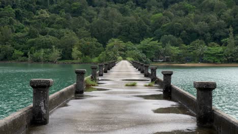 static shot of a concrete pier in the ocean after rainfall with green lush forest in the back