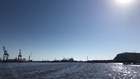 slow motion clip of an industrial dock harbor with containers and cranes on the background and a beautiful blue sky with some seagulls and the sea with waves