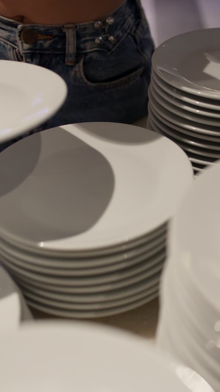 Server arranges stacks of clean white plates in softly lit restaurant buffet preparation area