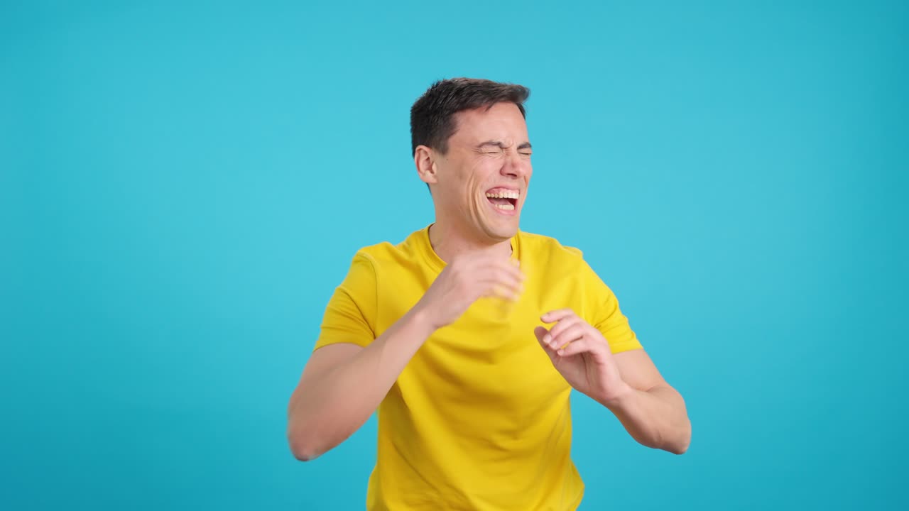A man in a yellow shirt laughing against a blue background