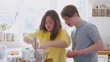 una pareja joven con síndrome de down mezcla ingredientes para una receta de pastel que están horneando en la cocina en casa.