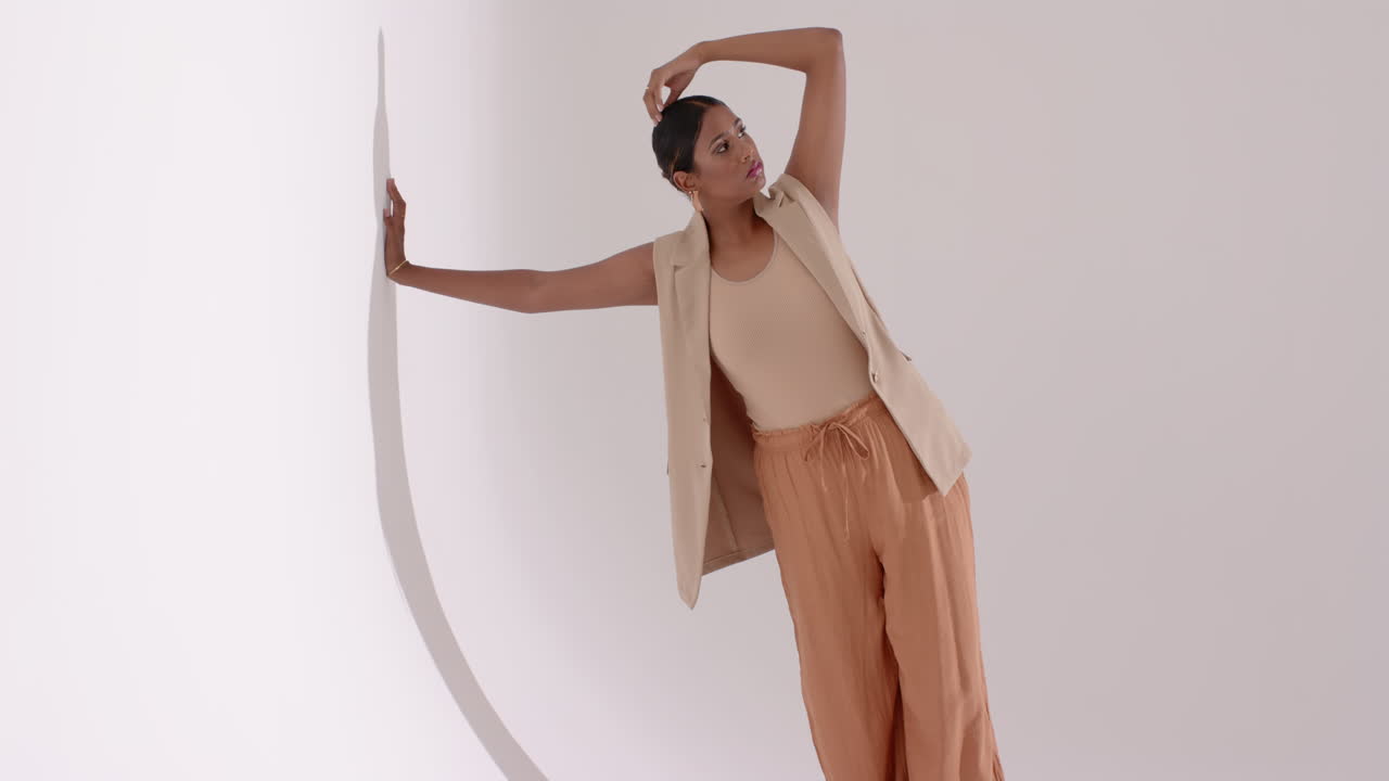 Touching arch prop Indian female model posing in beige outfit against white backdrop fashion shoot