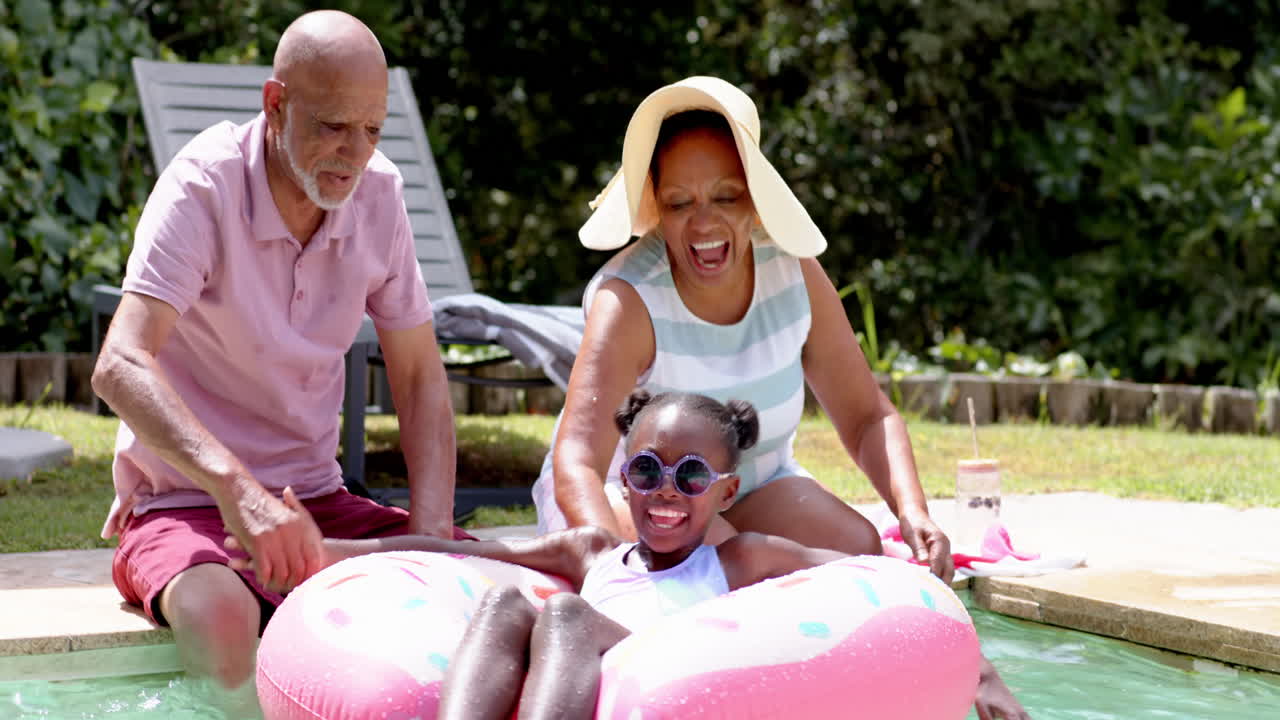 Diverse grandparents enjoying pool time with granddaughter on inflatable float, all smiling