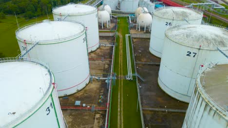 aerial drone revealing shot footage flying over backwards above large white storage tanks in a seaside industrial harbor or port area that contain oil or gas. small and large containers visible