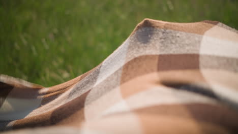 a little boy in a white shirt walks into a flowing plaid scarf in a sunny grassy field. another child, whose face is not visible, holds the scarf as the boy smiles with joy