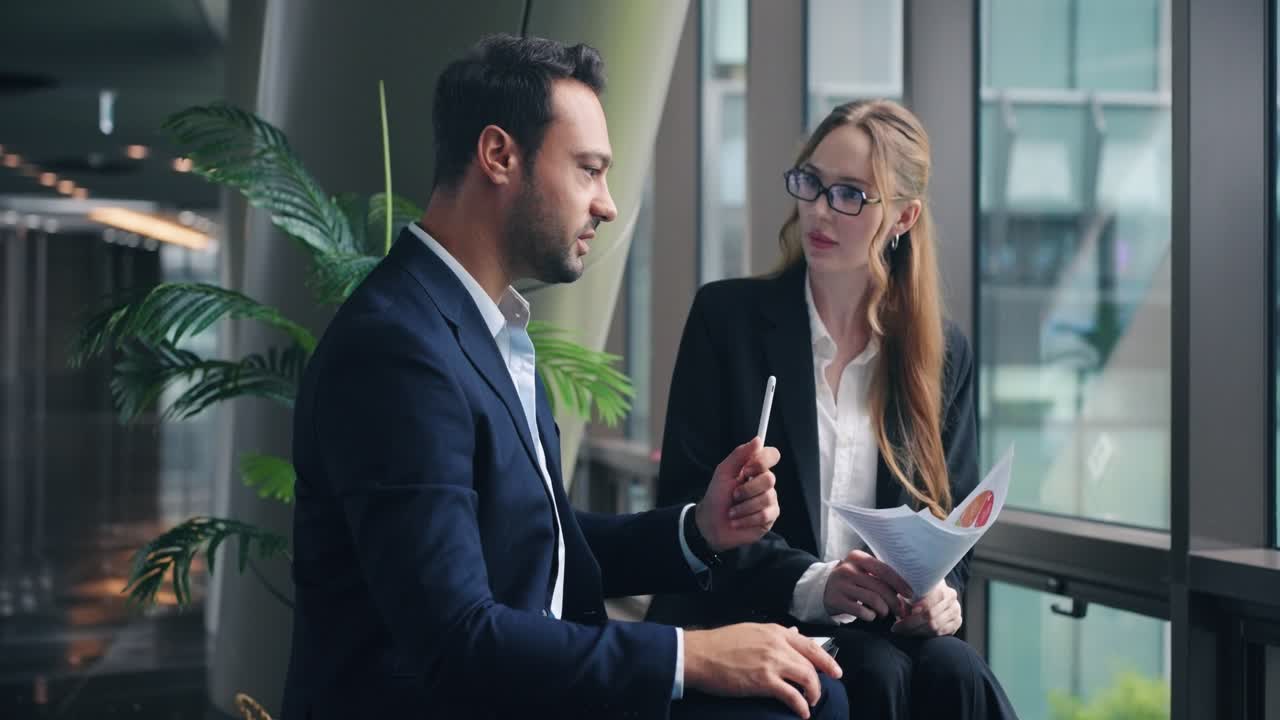 To professionelle erhvervsfolk gennemgår finansielle dokumenter og taler engageret under et møde i et moderne kontor.