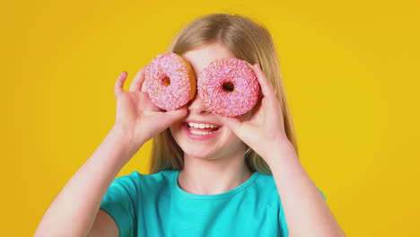 studio portrait of girl holding two donuts in front of eyes against yellow background