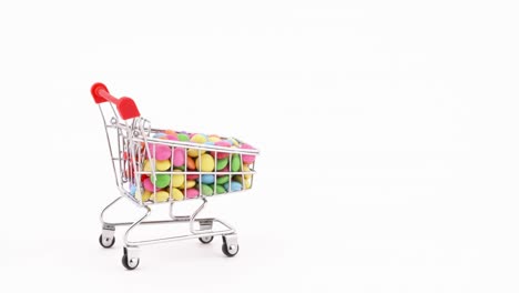 el carrito de compras lleno de dulces caramelos de chocolate de colores se mueve en el marco. aislado en el fondo blanco.