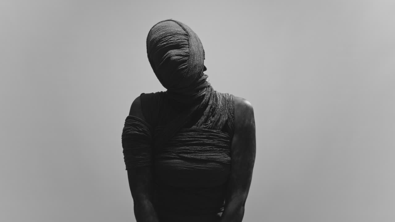 A mummy of a woman on a white backdrop slowly turns her head