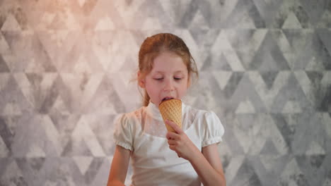 white girl in white outfit enjoying ice cream cone while focusing attentively on something in front, standing indoors against textured gray geometric wall
