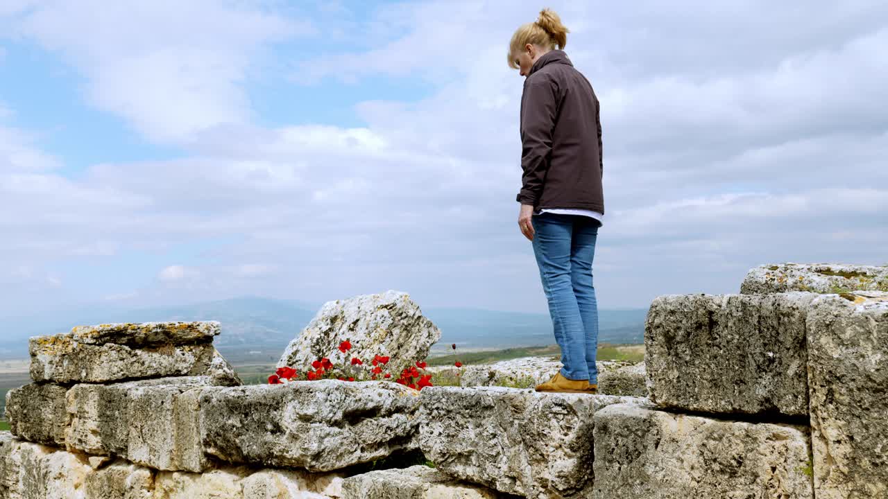 Woman climbs carefully over ancient stone ruins to discover wild red poppies
