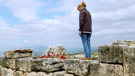 woman climbs carefully over ancient stone ruins to discover wild red poppies