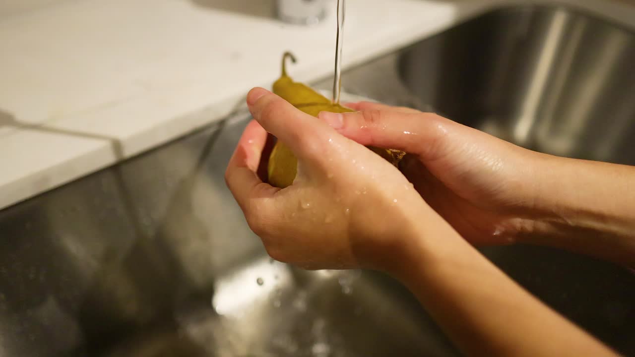 Manos lavando una pera bajo agua corriente
