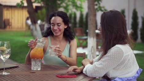 personas, comunicación y concepto de amistad - mujeres jóvenes sonrientes bebiendo jugo de naranja y hablando en una cafetería al aire libre, sonrientes