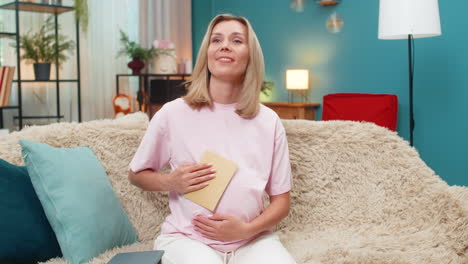 pregnant woman writing message to baby placing envelope on belly imagining future reading warm hope