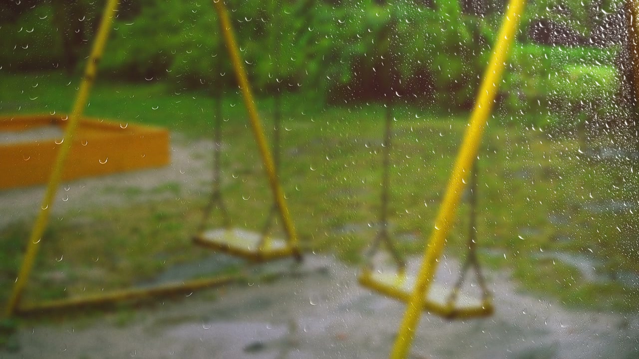 Swing during the rain. View from the window. Raindrops on the glass.