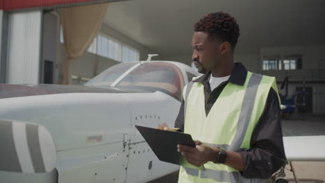 black inspector checking aircraft exterior and taking notes outside hangar