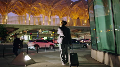 Suit-man-calling-phone-dark-street-back-view.-Business-traveler-pulling-suitcase