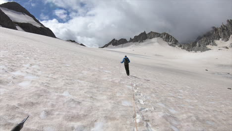 一名登山者正在雪地覆蓋的冰川上行走, 靠近岩石尖峰, 一根绳子绑在他身上,