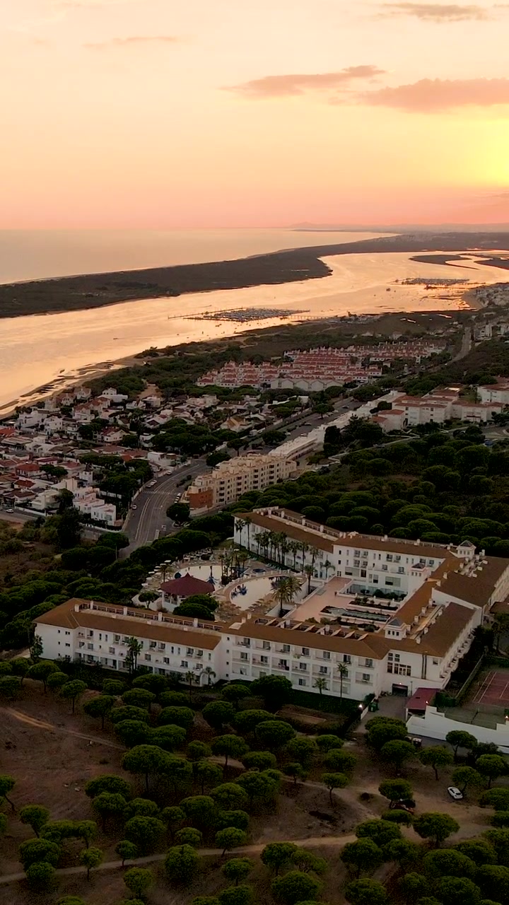 Tomada aérea cinematográfica de um resort de luxo em El Rompido, Espanha, durante um pôr do sol na hora dourada, com o rio e a costa