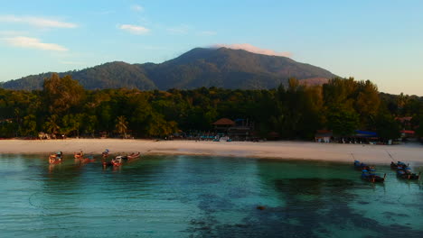 Shot-of-seaside-from-above-using-drone-with-white-sand-beach,-green-trees-and-mountain-in-the-background