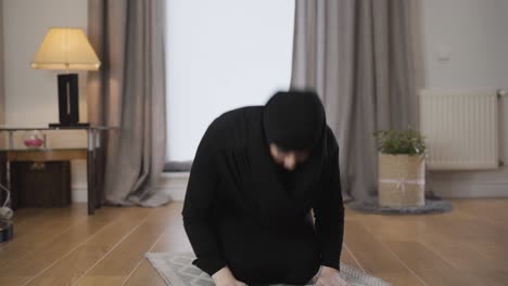 portrait of young muslim woman in black traditional hijab bowing down and raising up. eastern woman praying at home. eastern culture, religion, lifestyle.