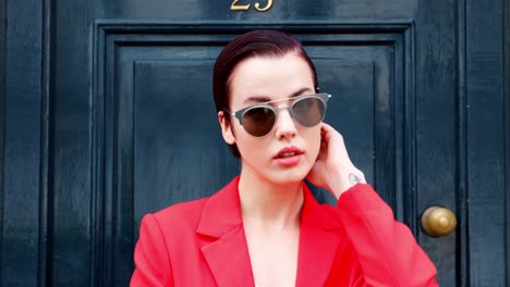 mujer elegante con gafas de sol de pie fuera de la puerta azul